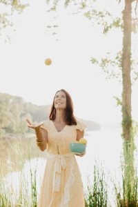 Photo of author Andi Holyfield outdoors with a bowl of fresh oranges tossing one into the air